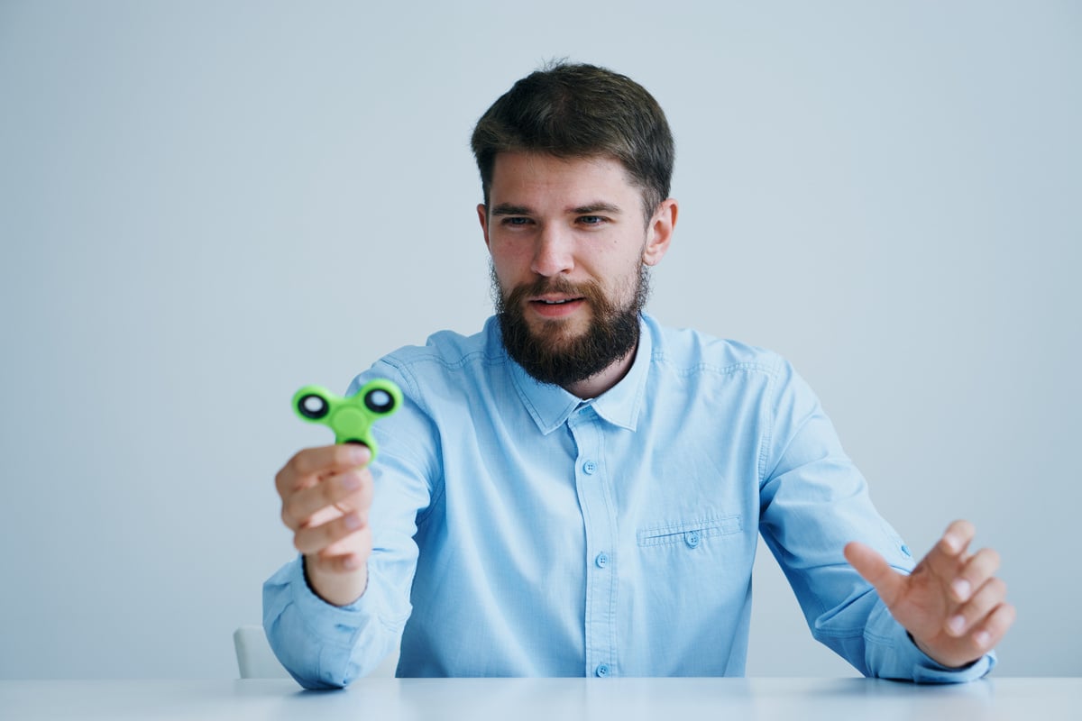 A Bearded Man Sits at a Table with a Spinner in His Hand a Toy against Stress Relaxation
